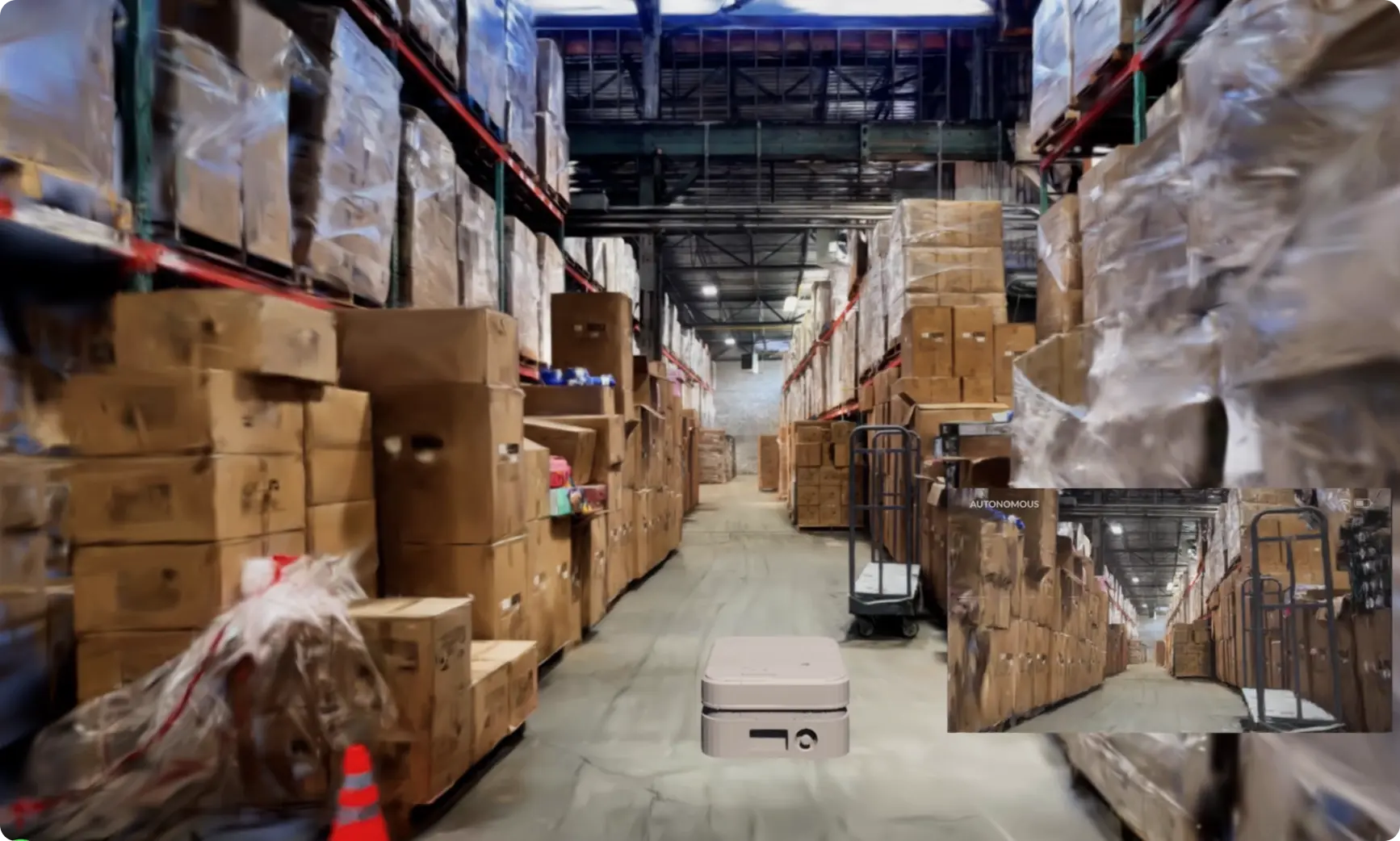 Autonomous mobile robot moving through a warehouse aisle with a live camera feed inset
